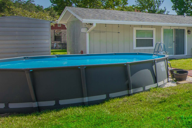 Above ground pool on grass in front of house.