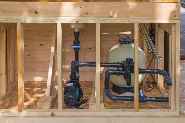 Swimming pool sand filter and pump system in a timber enclosure.