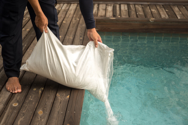 Man pouring a bag of pool salt into a swimming pool.