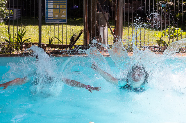 Two girls jumping into the pool and splashing.