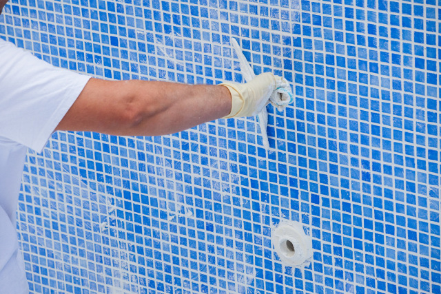 Repair man applying grout to pool tiles.