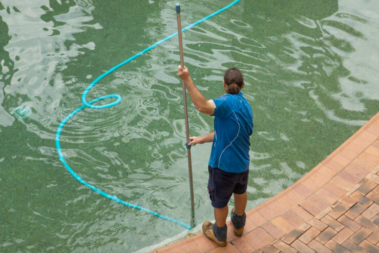 Man manually vacuuming a swimming pool.