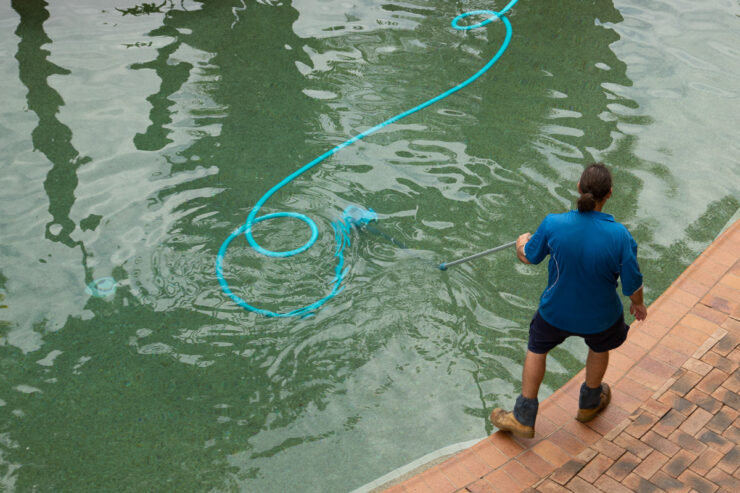 Man vacuuming a swimming pool with a telescopic pole.
